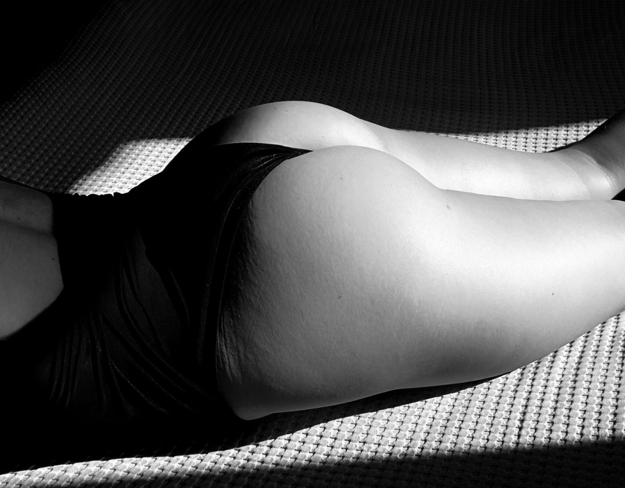 A woman's naked legs and butt stretching out across a sofa in black and white.