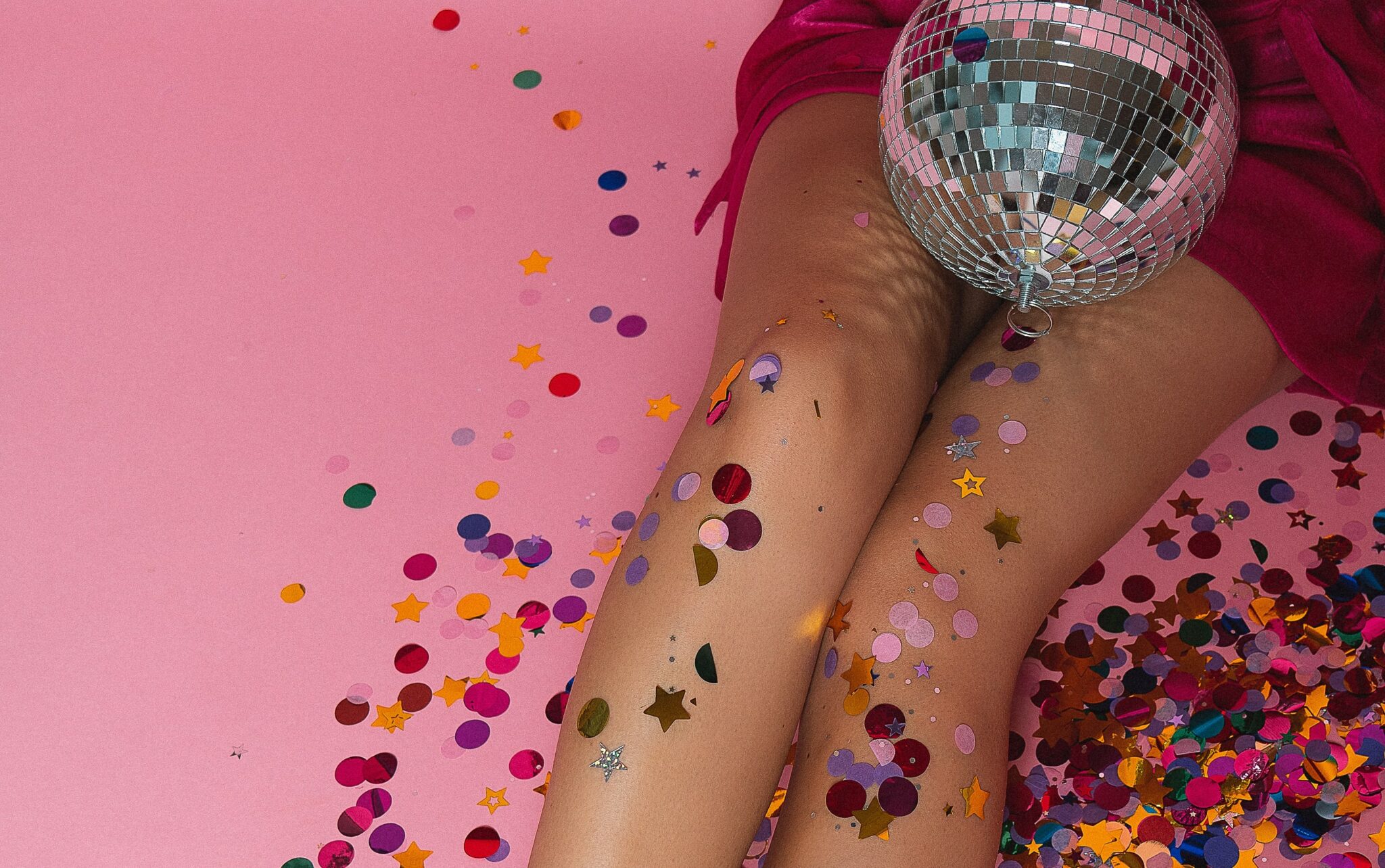 A woman sitting in confetti with a disco ball sitting in her lap.