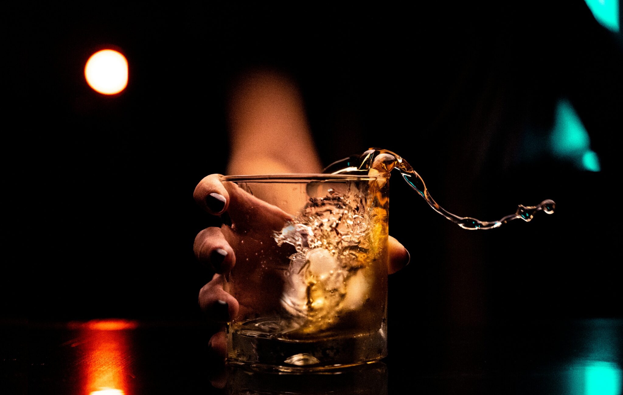 Alcohol splashing out of a glass in a dark room.