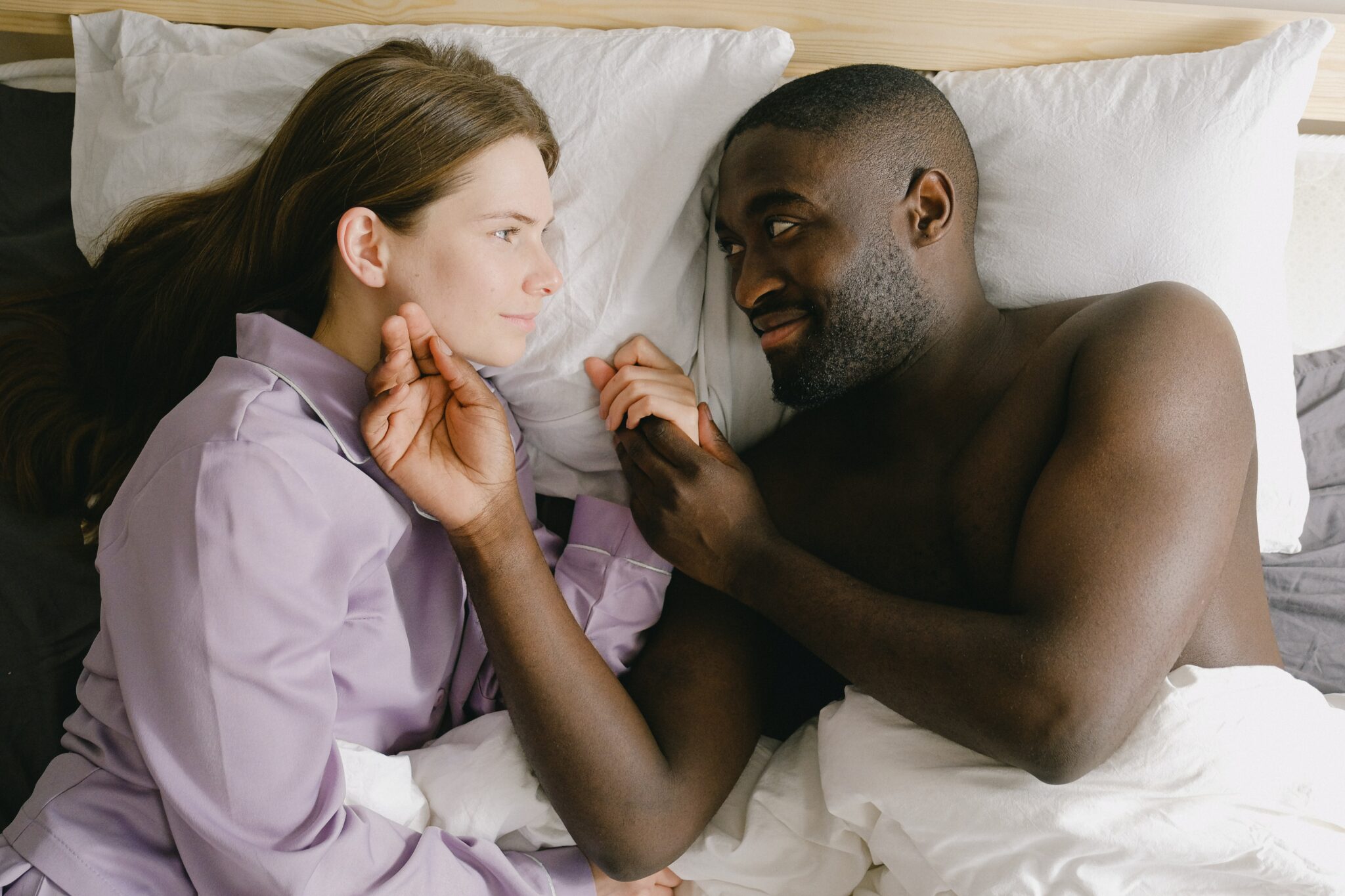 A couple laying in bed, the man holding his partner's face.