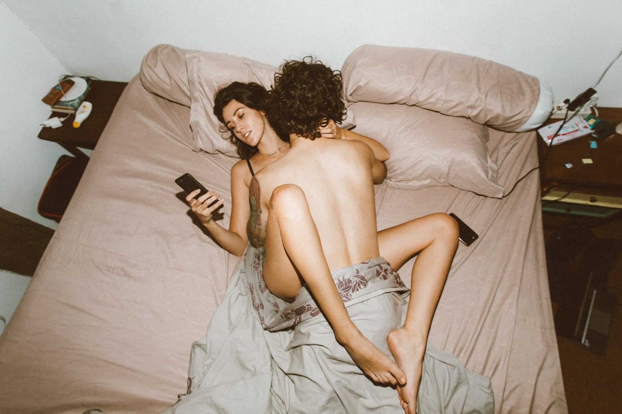 A couple having sex in their bed while the woman looks at her phone.