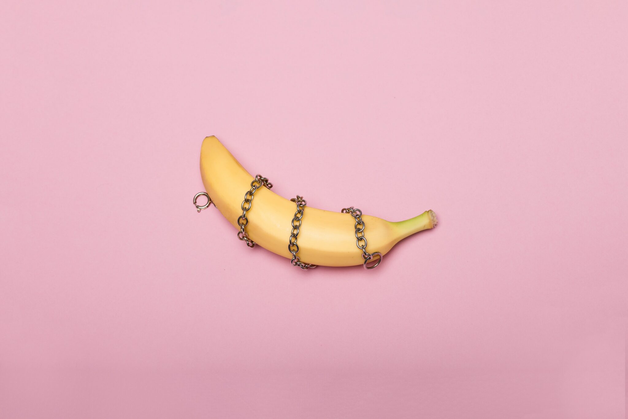 A banana wrapped in a chain over a pink background.