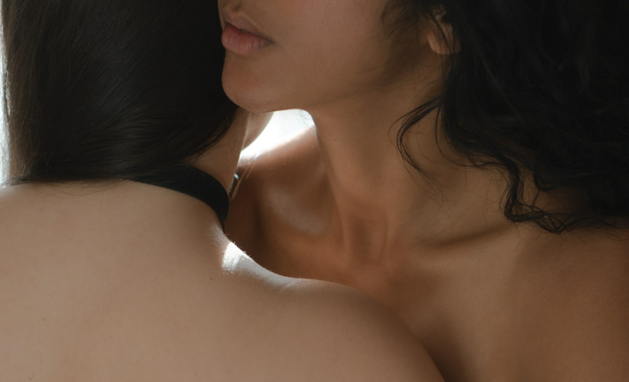 A close-up of a woman whispering in another woman's ear.