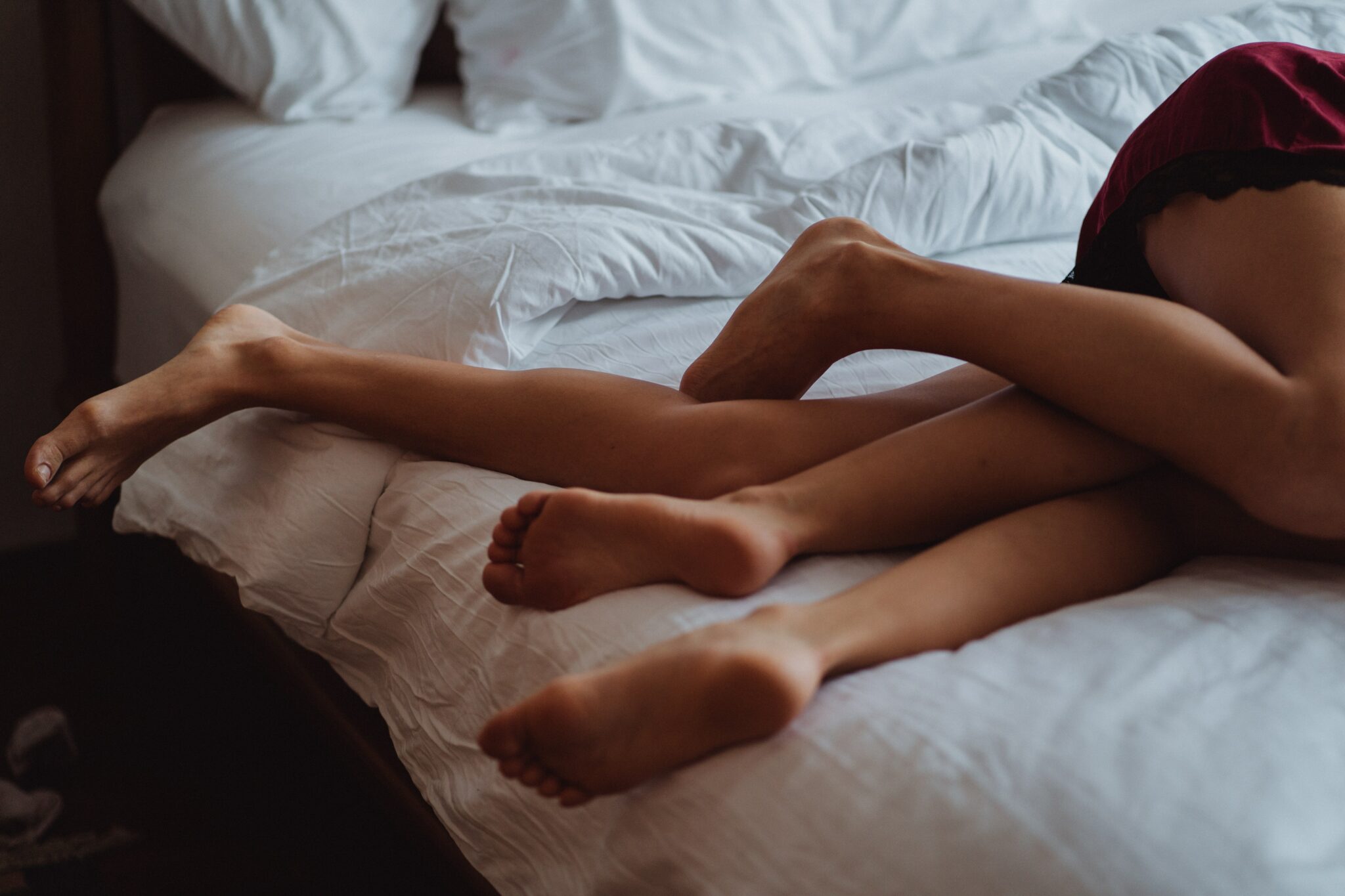 Two women cuddling on a bed with their legs intertwined.