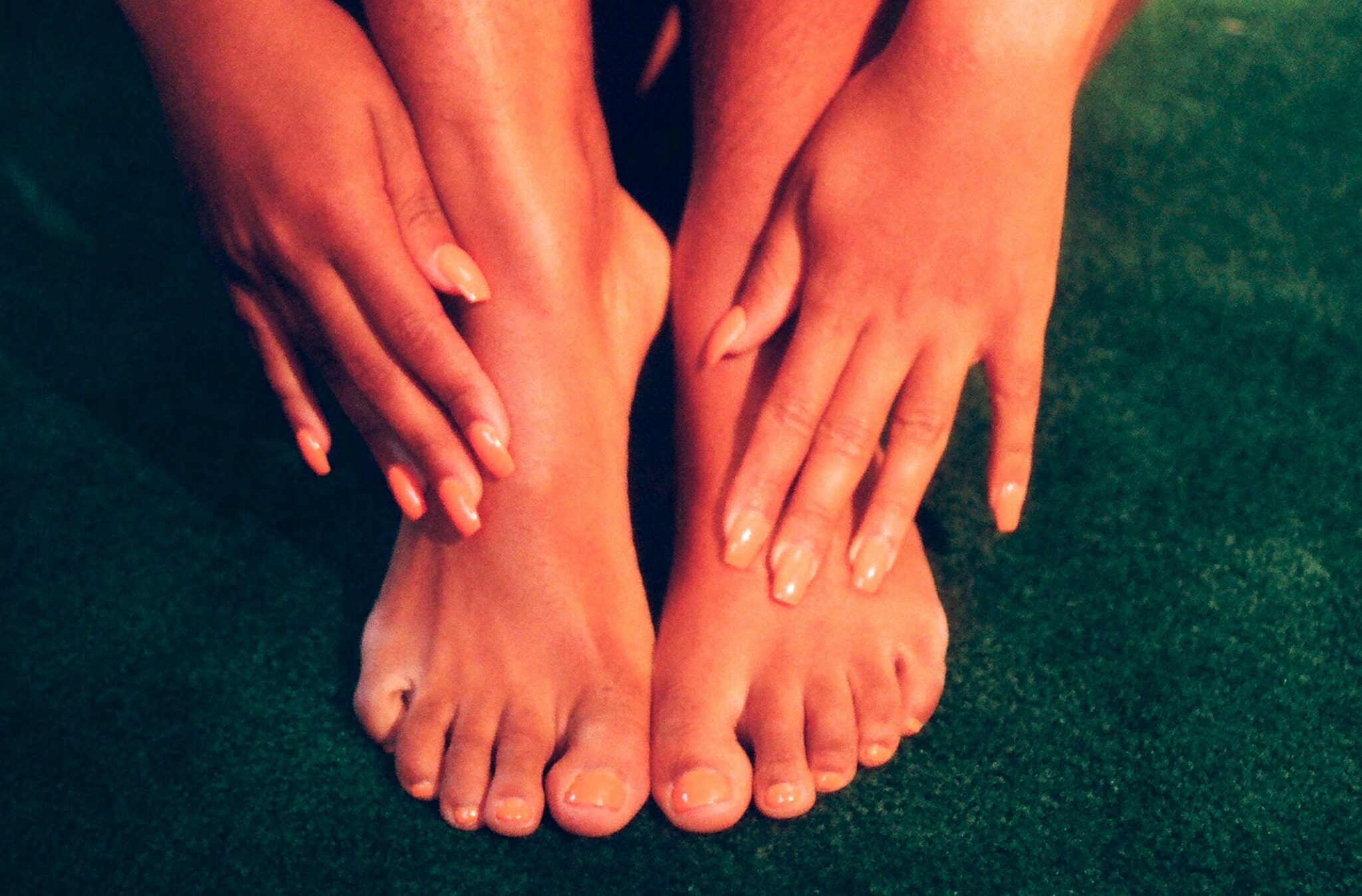 A woman rubbing the tops of her feet with manicured hands.