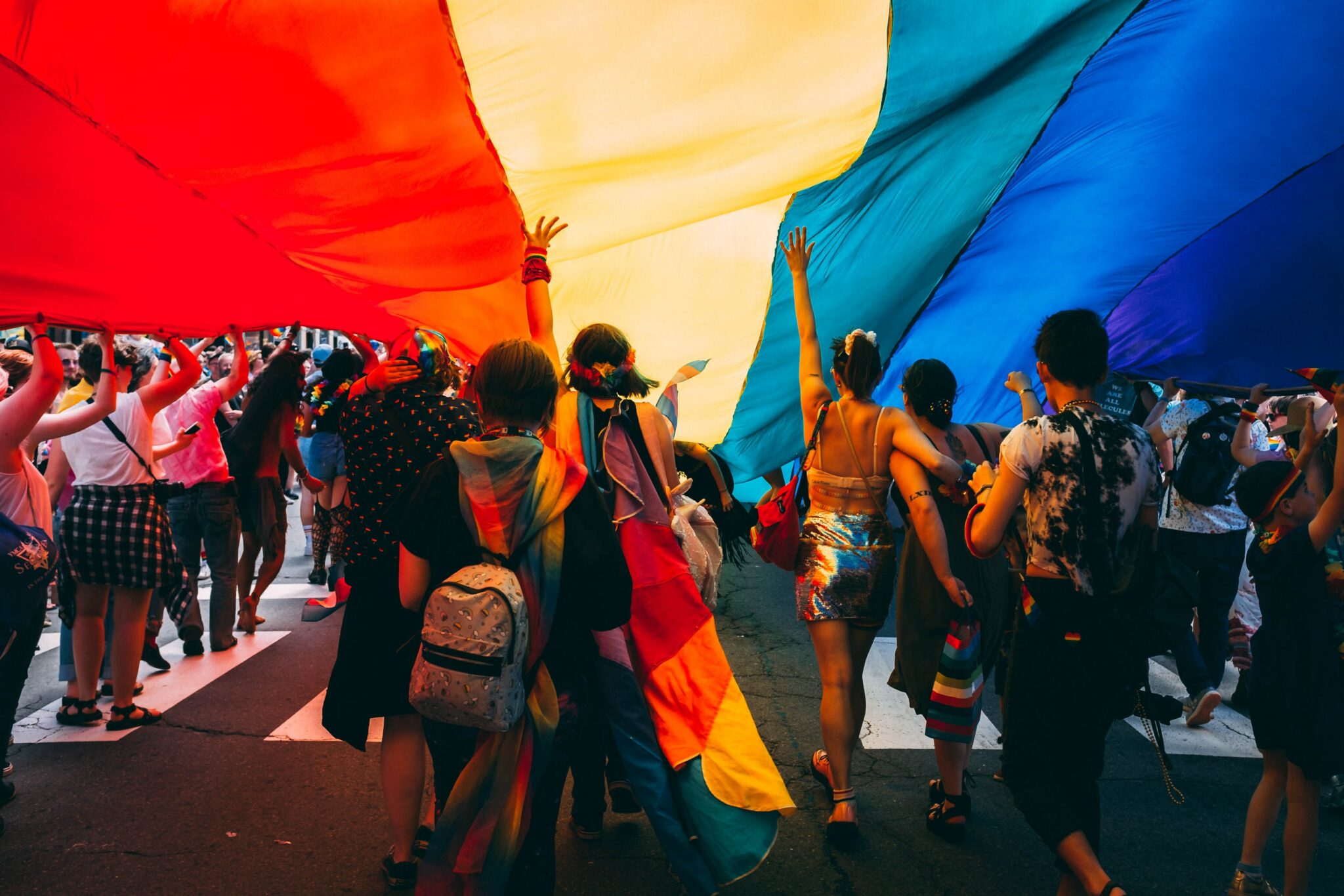 A group of people standing under a large rainbow flag at a Pride parade.