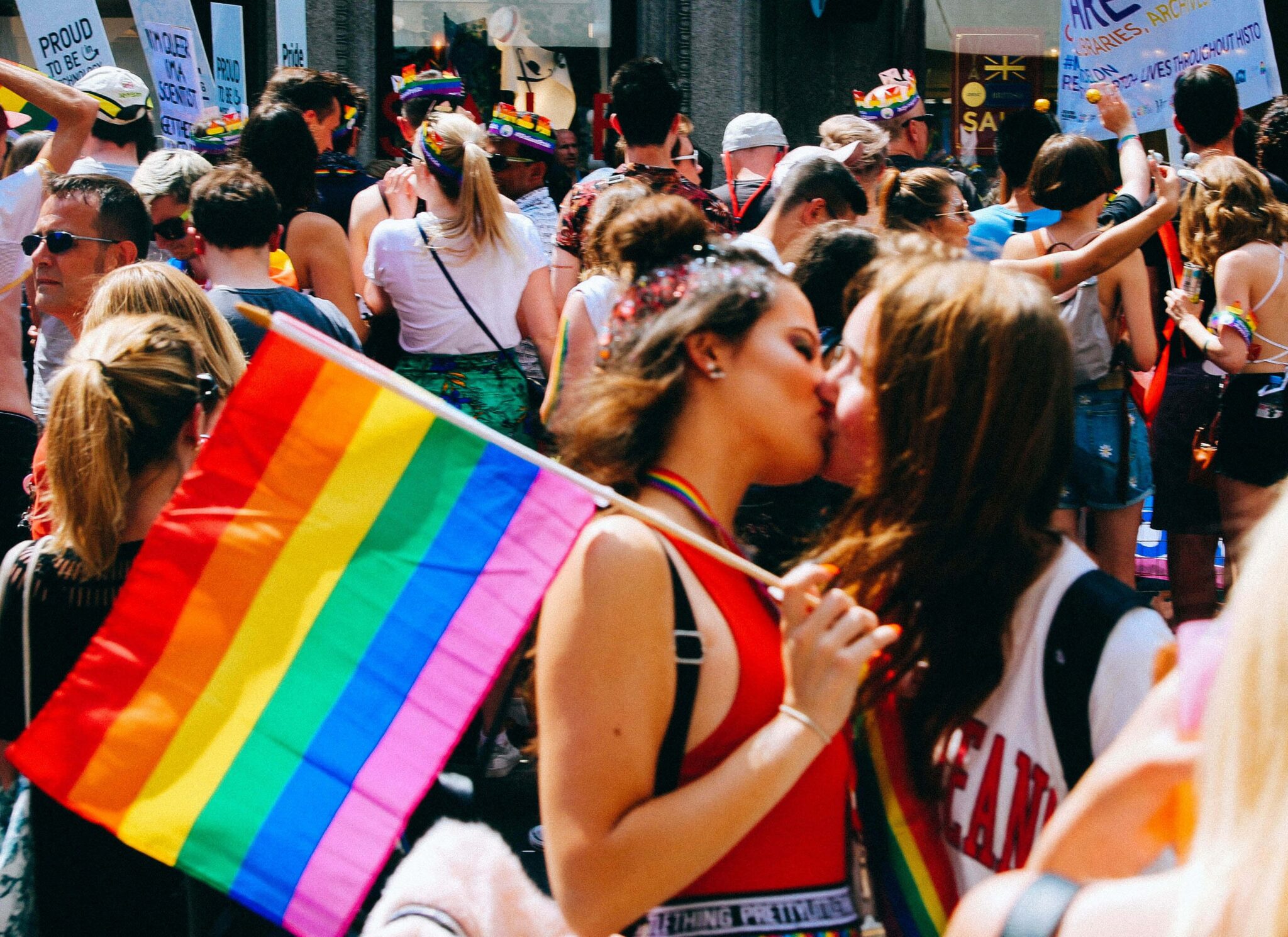 Two women at a Pride parade kissing and holding a flag.