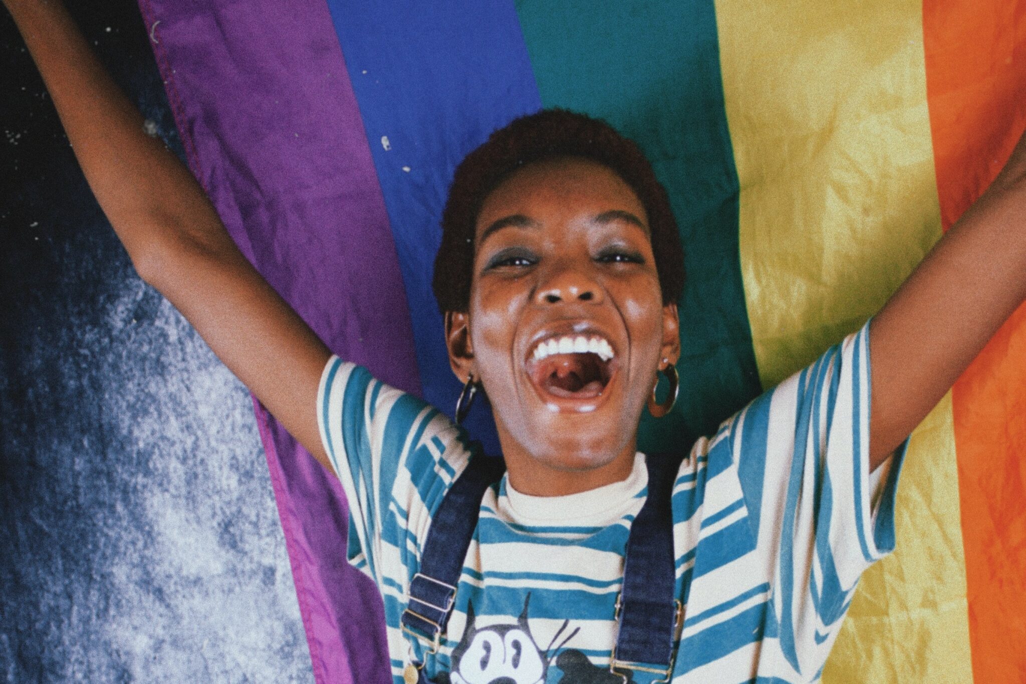 A Black woman holding a rainbow flagging and smiling widely.