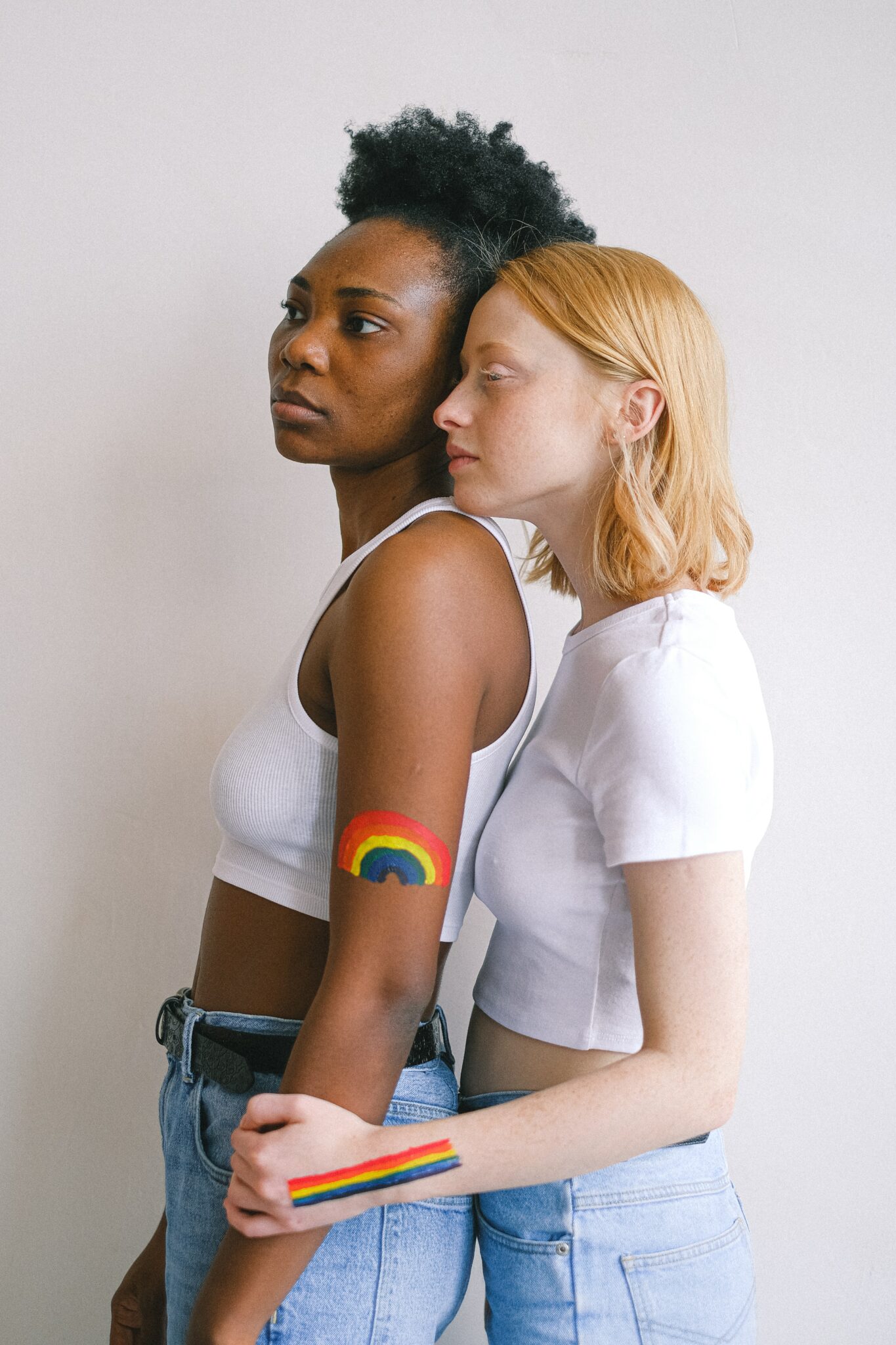 Two women, standing and hugging with rainbows painted on their hands.