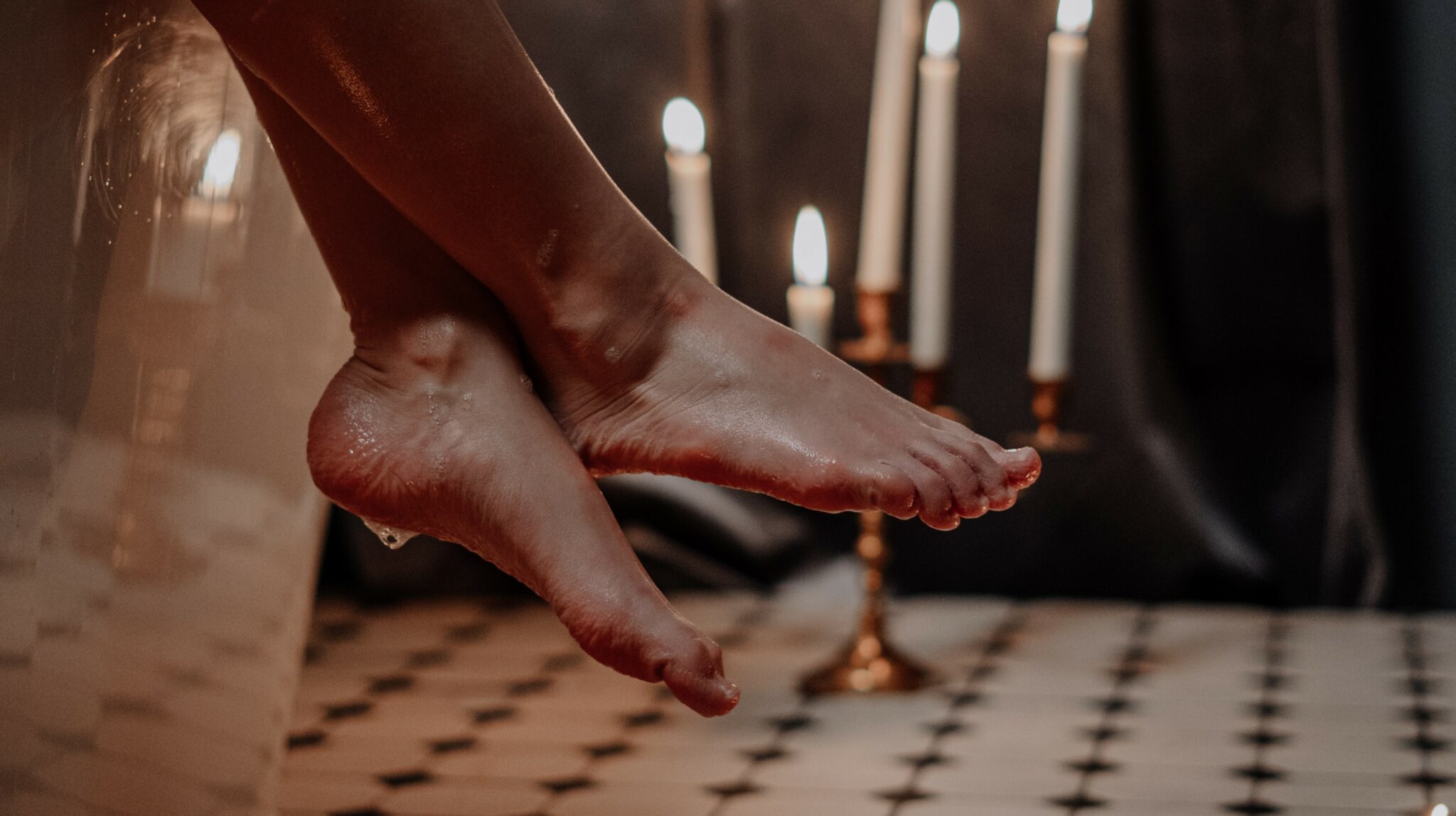 Woman's feet dangling off the side of a bathtub with a lit candelabra in the background.