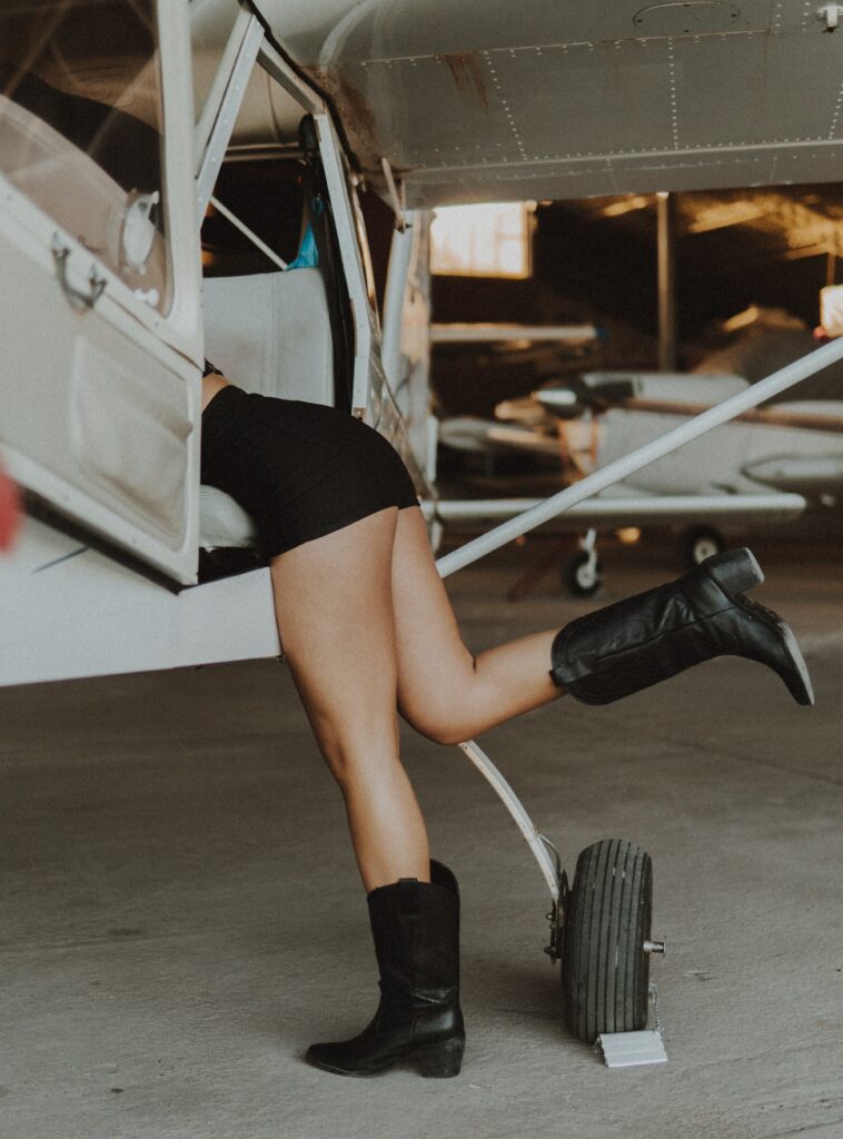 A woman reahing into an airplane wearing a short, black skirt and black boots.