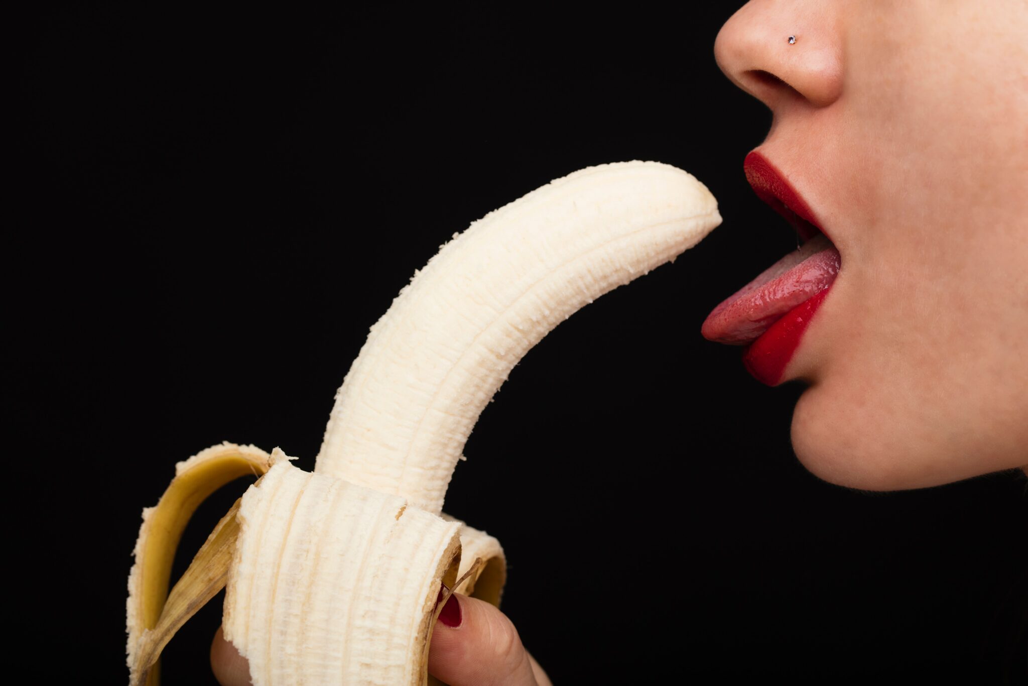A woman holding a banana to her open mouth and tongue.
