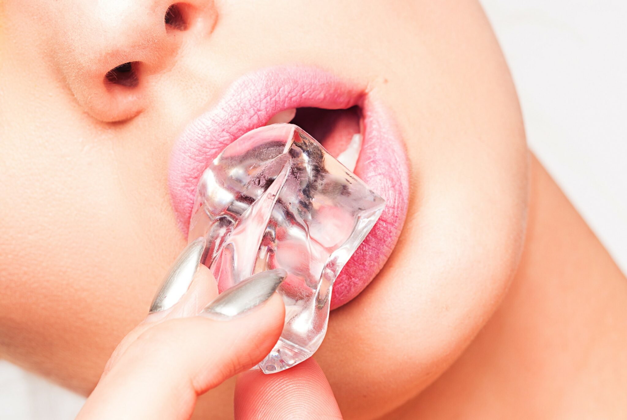 A woman holding an ice cube between her lips.