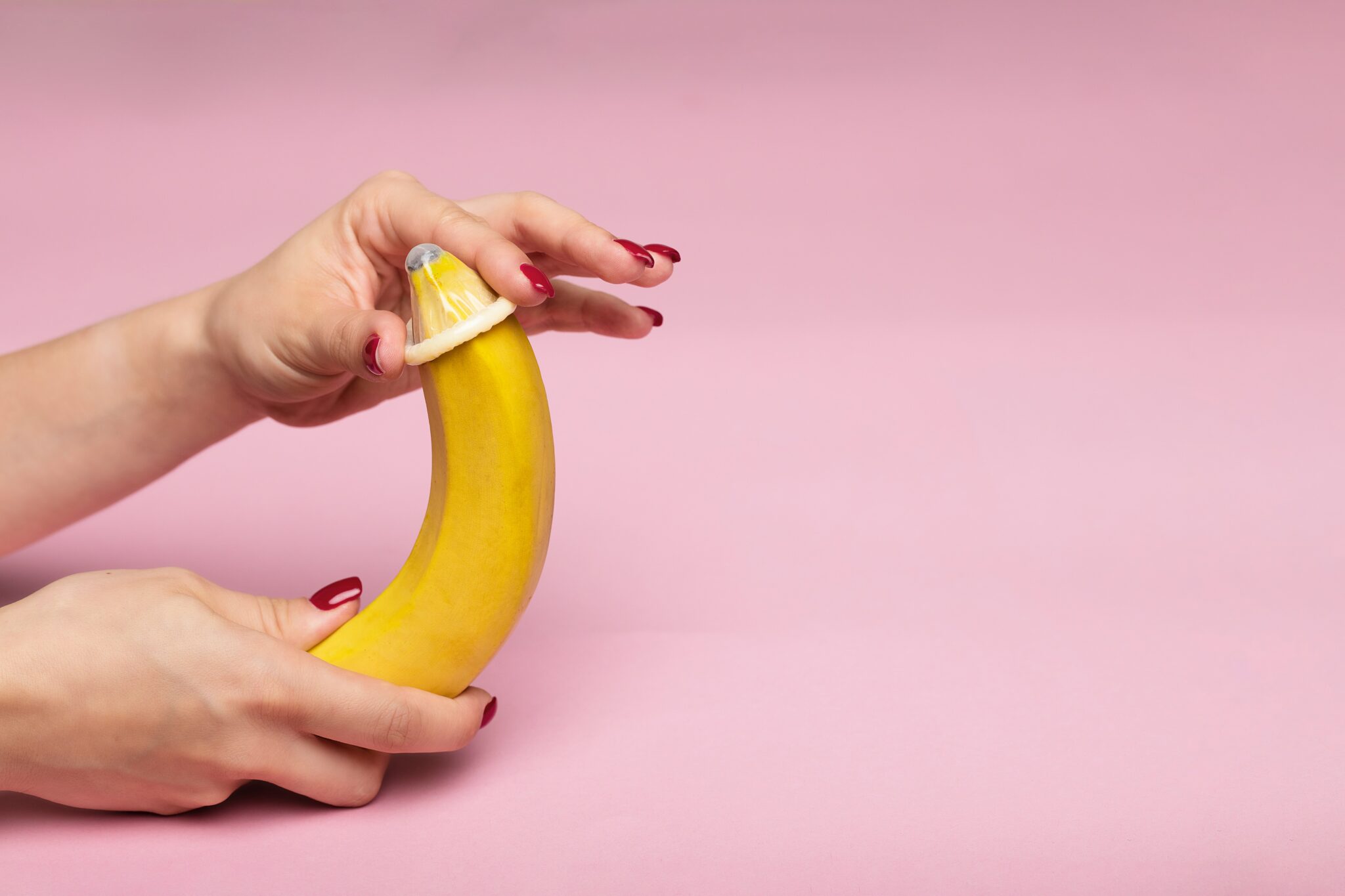 A woman's hand sliding a condom onto a banana.