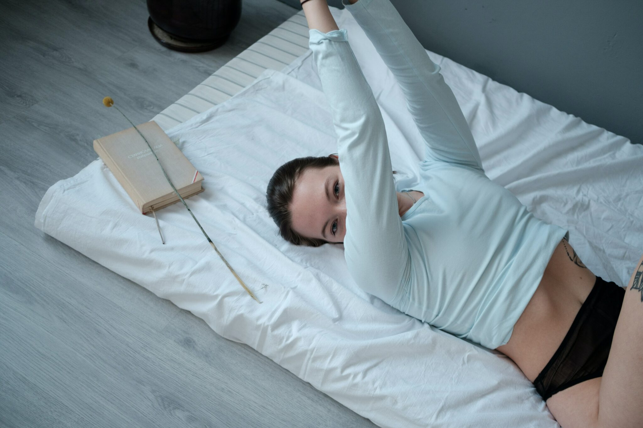A woman laying on a white blanket, looking at the camera and wearing a white long sleeve shirt and black panties.