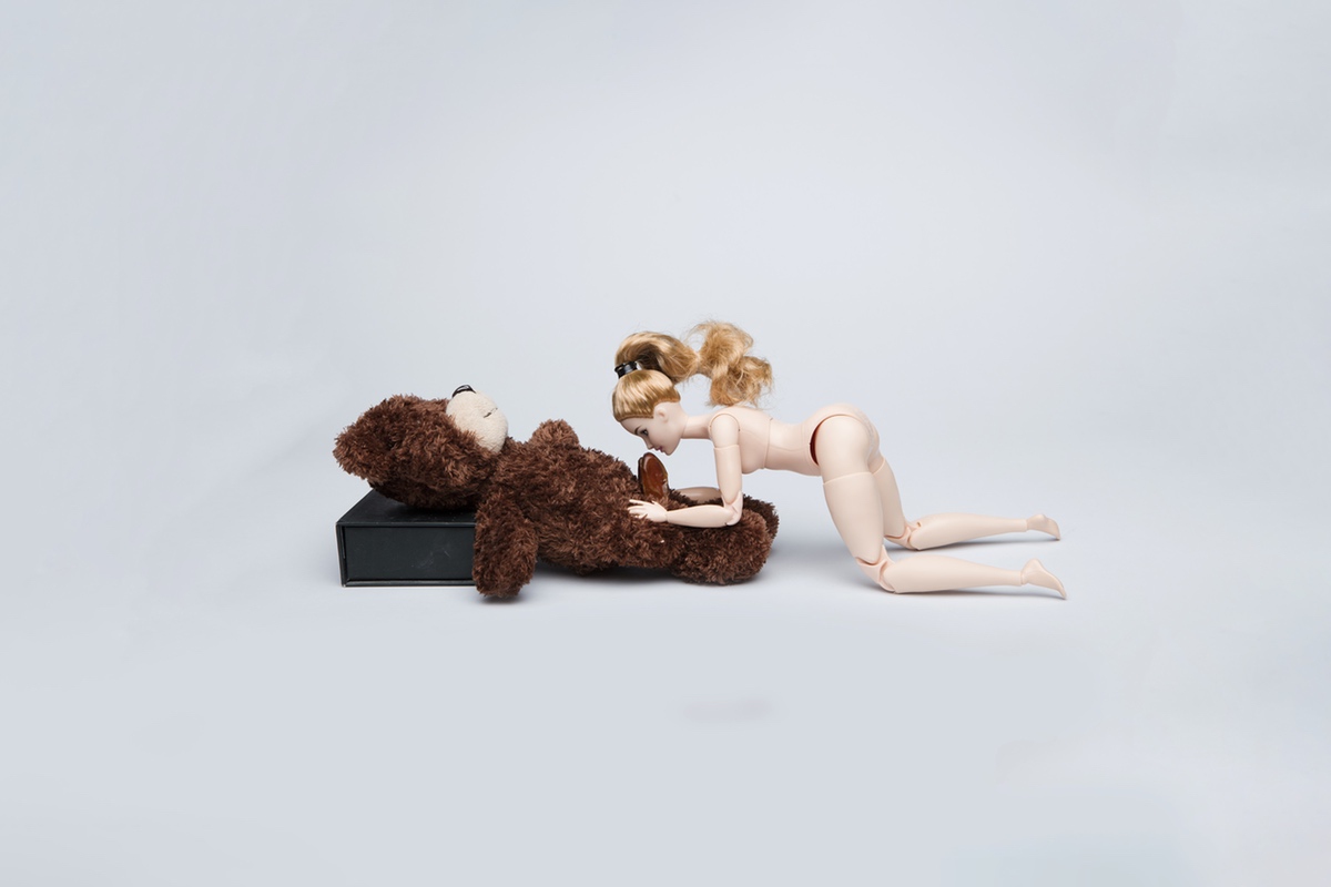 A naked Barbie doll giving a blow job to a small stuffed bear.