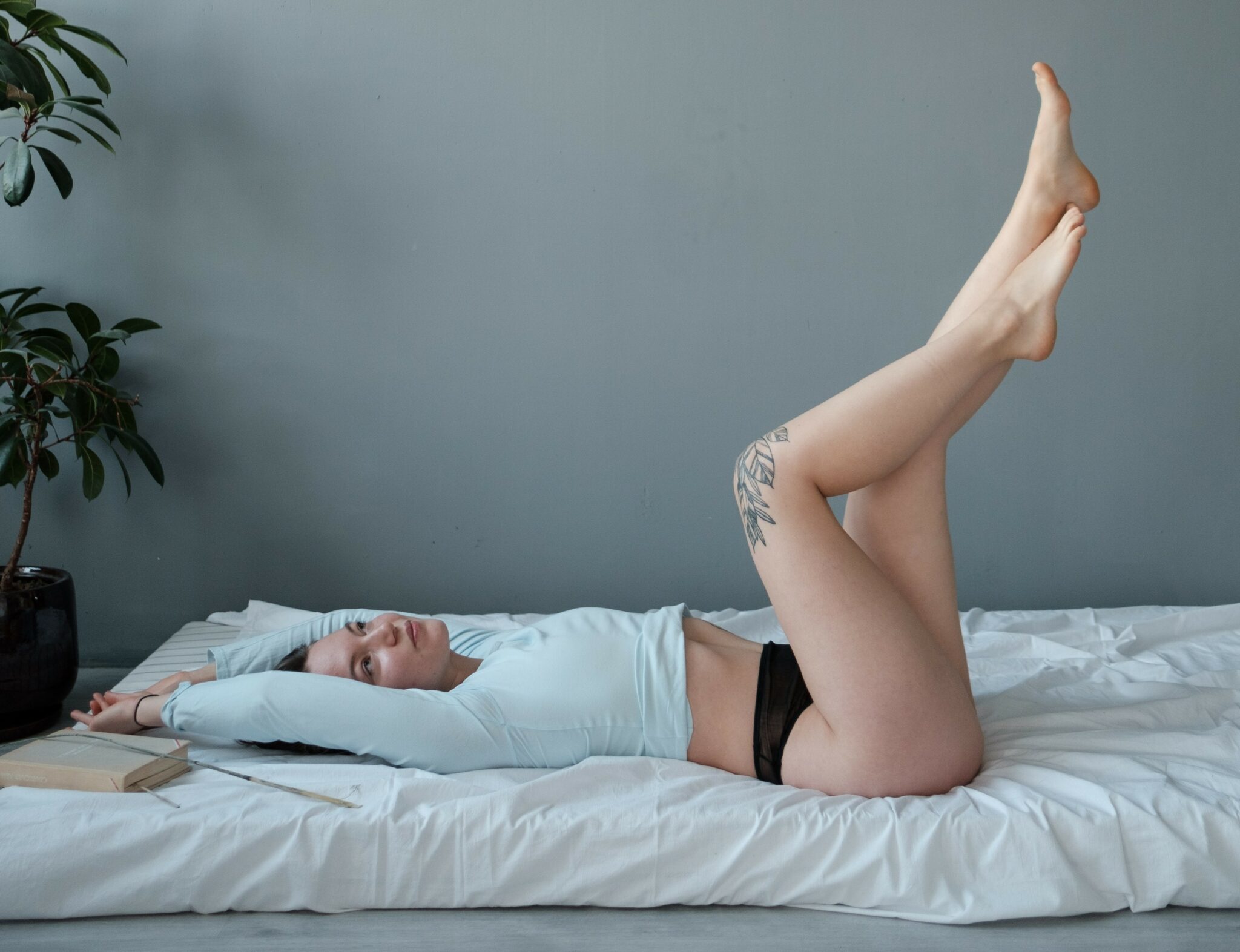 A woman posing on her bed in black underwear and a white long sleeve shirt, her legs lifted in the air.