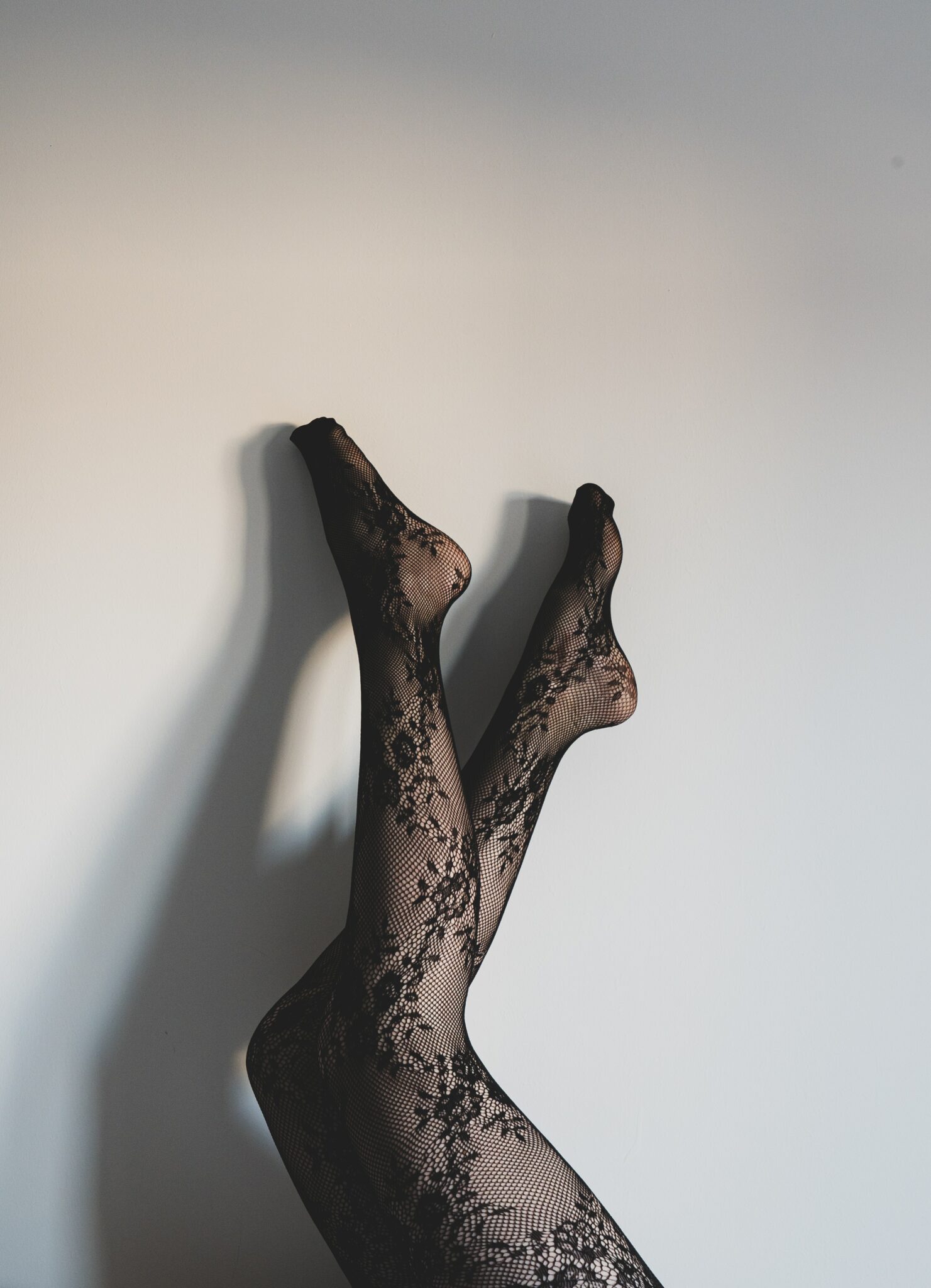 A woman's legs stretching up a wall in a pair of black lace stockings.