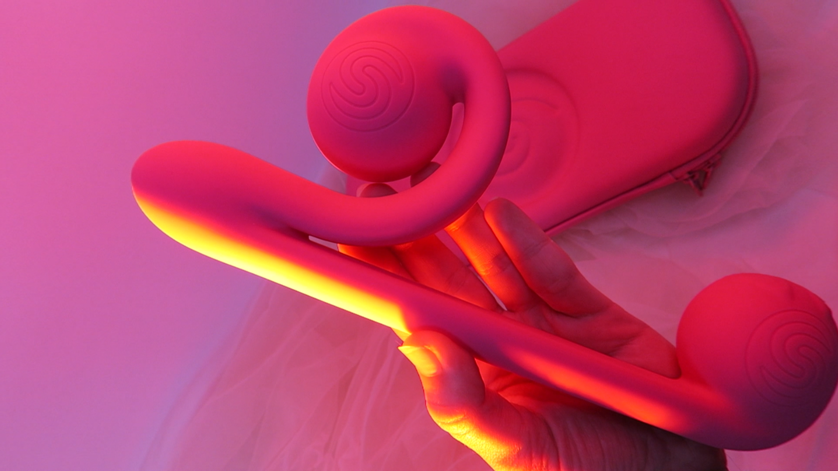 The Snail Vibe hot pink vibrator being held in low, pink lighting.