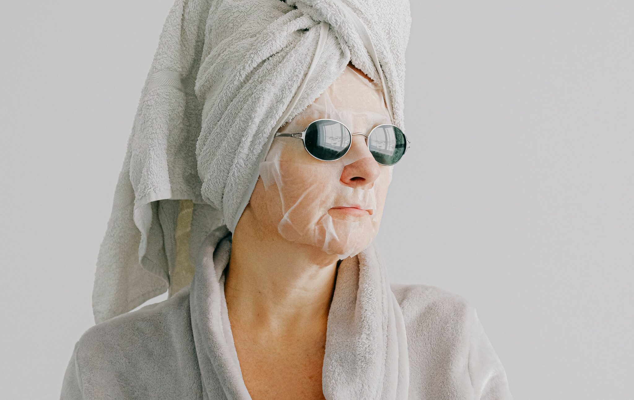 With a towel wrapped on her head, face mask and sunglasses on, an older woman stares outward.