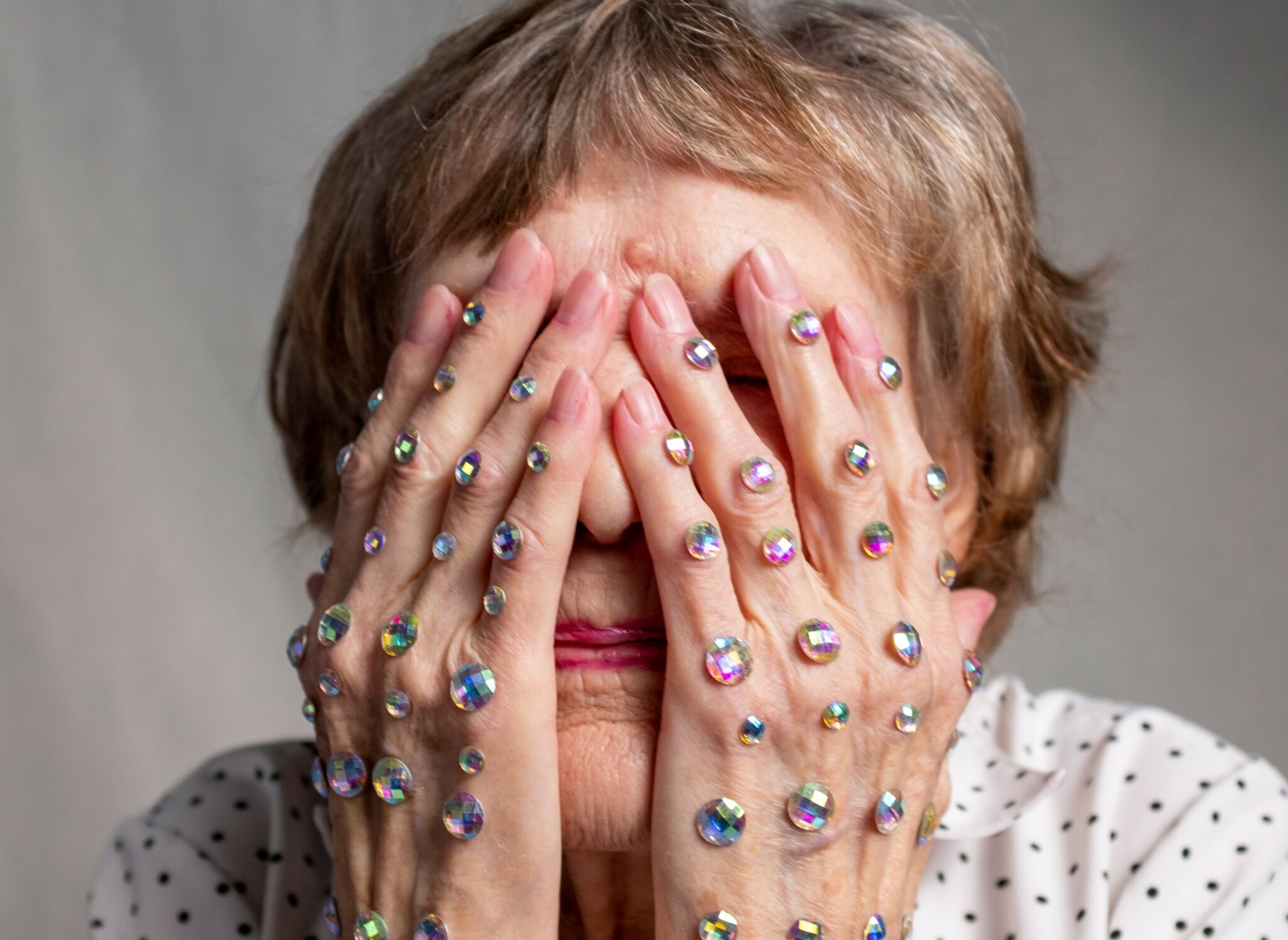 An older woman holding her face with rhinestone-covered hands.