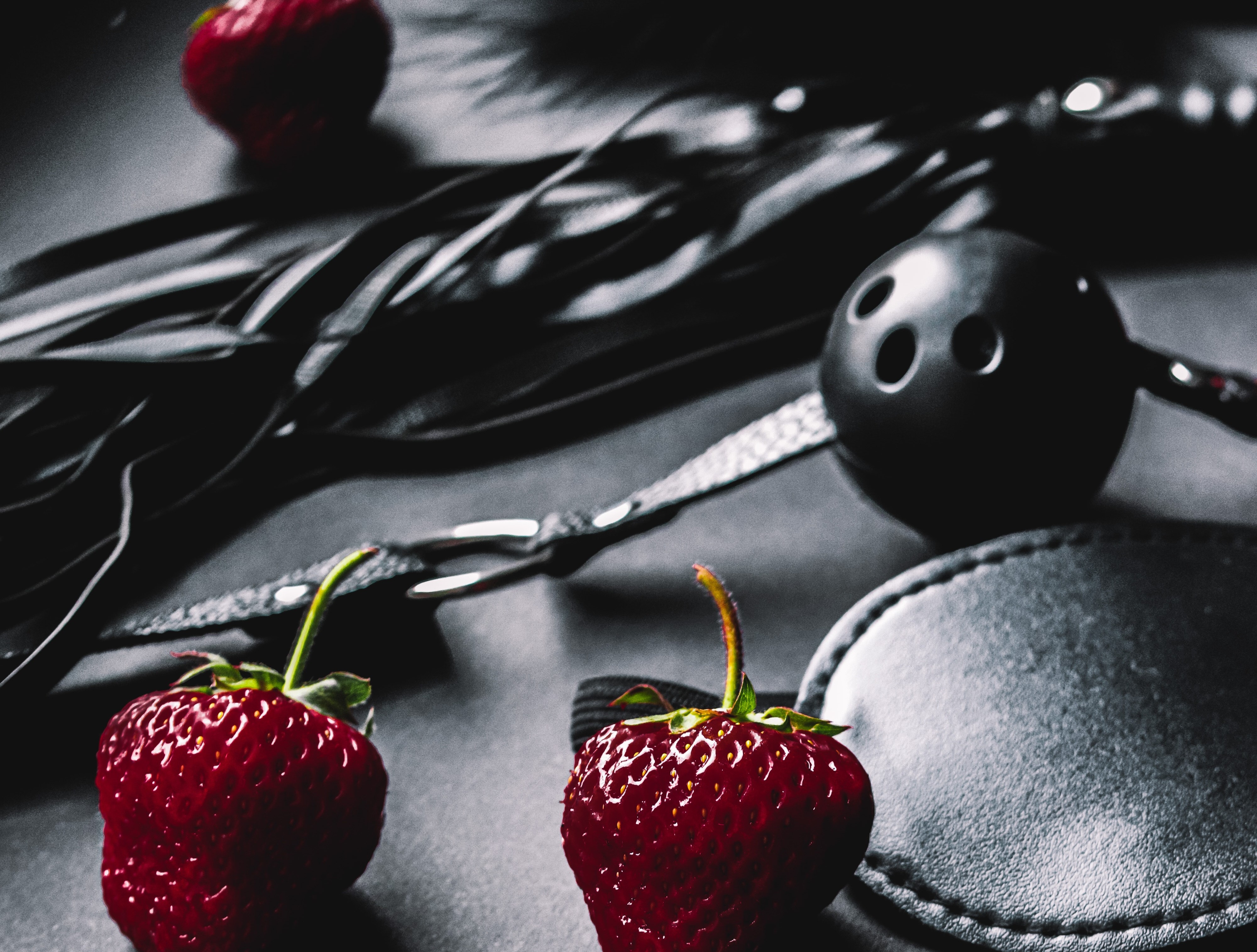 Black bondage toys laid out beside ripe strawberries.