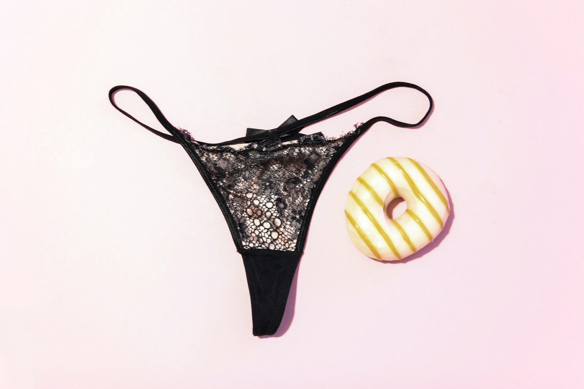 A pair of black lacy panties next to a donut.
