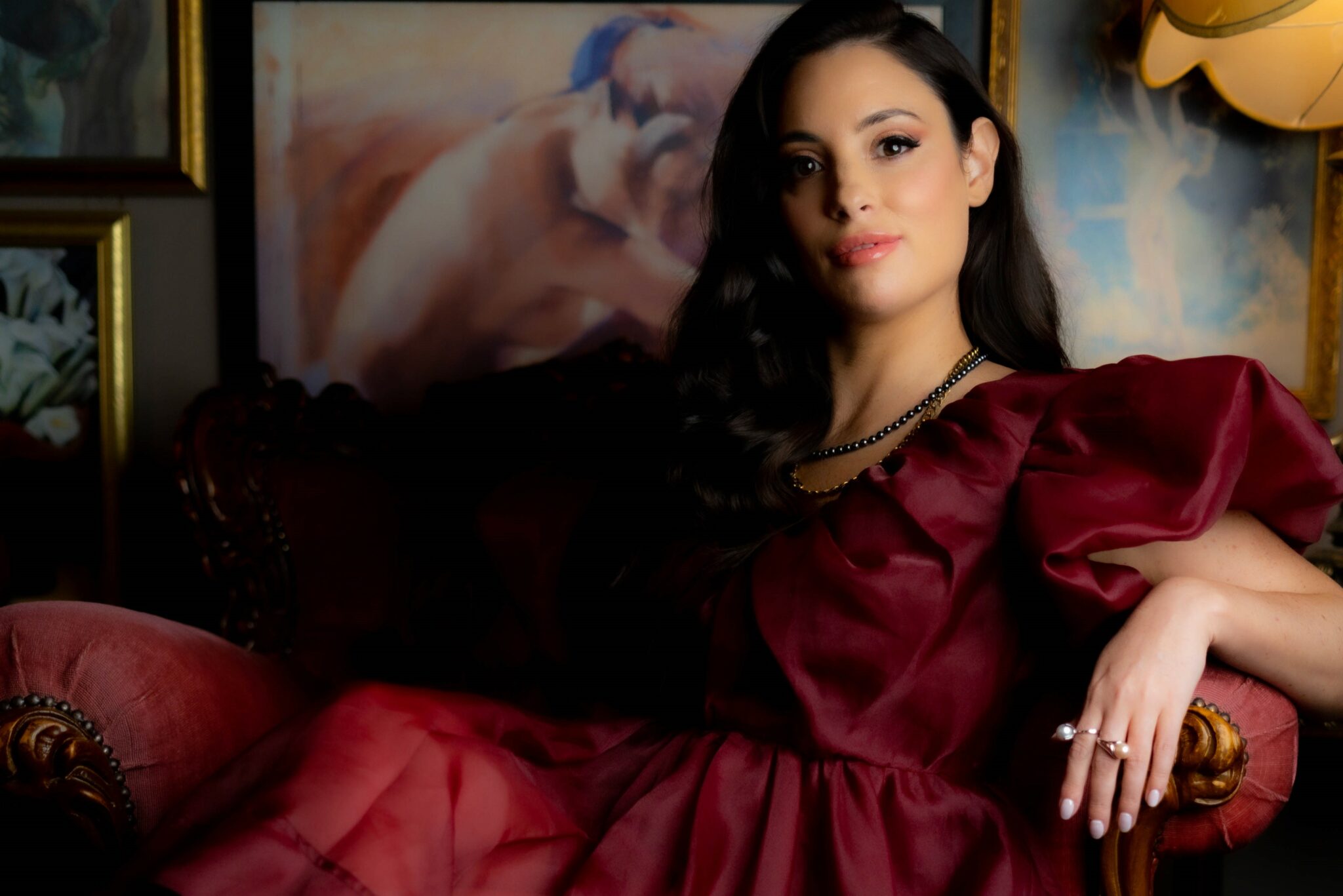Author Jade May reclines in an old chair wearing a stunning burgundy gown.