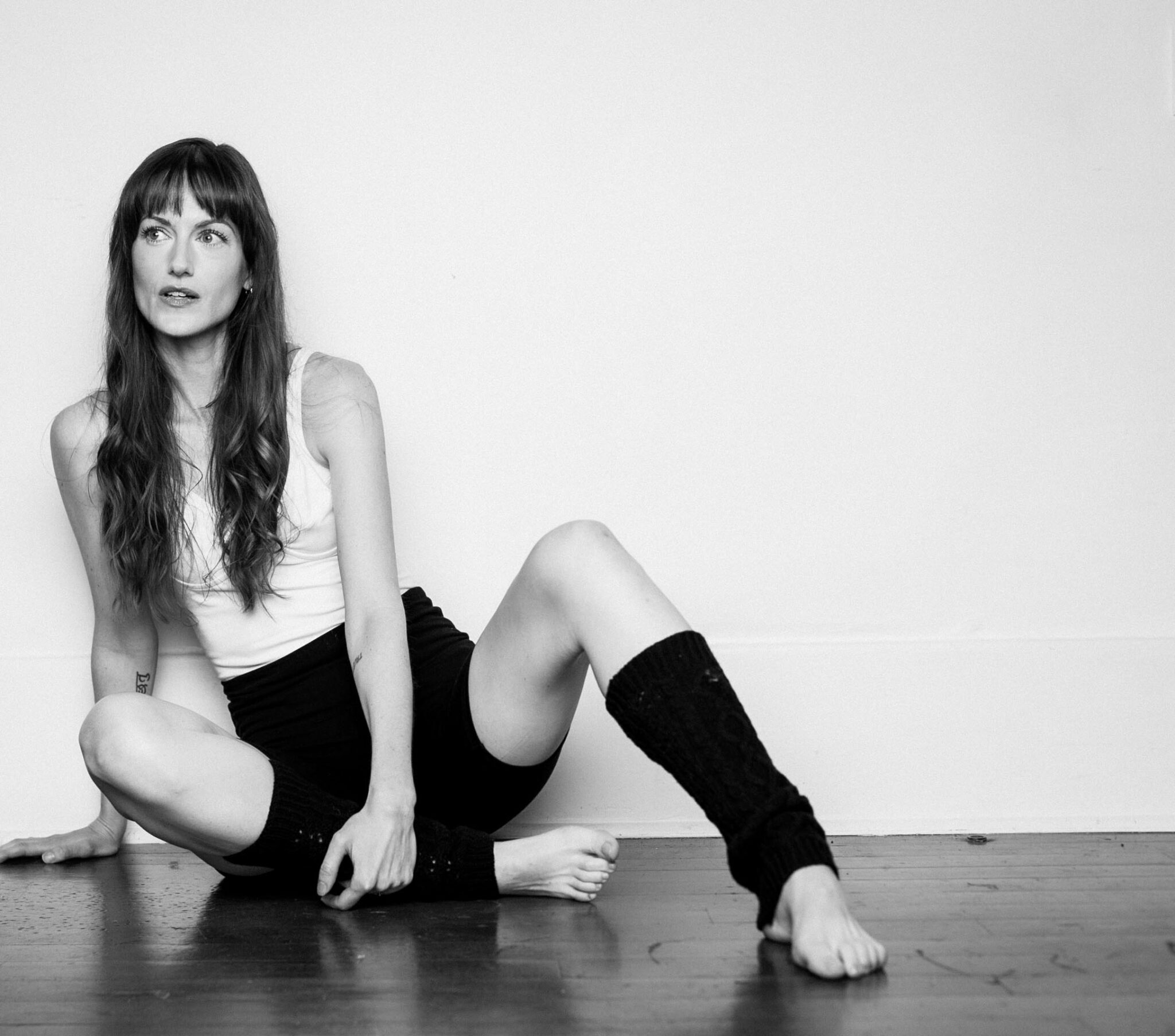 A full body image of Brianne Hogan sitting on the floor with one leg outstretched
