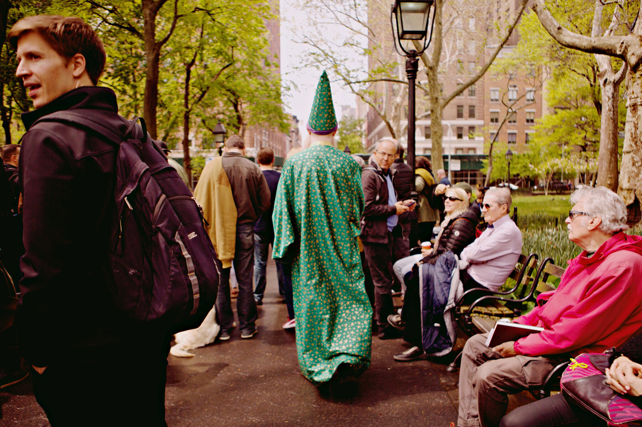 Devin the Wizard, wearing his green wizard hat and robe, walking through a crowd of people in the city.